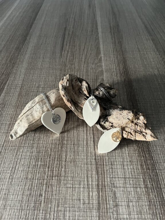 coeur et feuille en ceramique ornés de breloques argentées sur une chaine en acier inoxydable posés sur un support en bois flotté